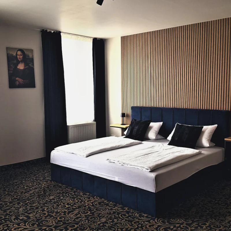 Doppelzimmer im Hotel In Amberg mit Doppelbett vor Holzlamellenwand und offener Zimmertür