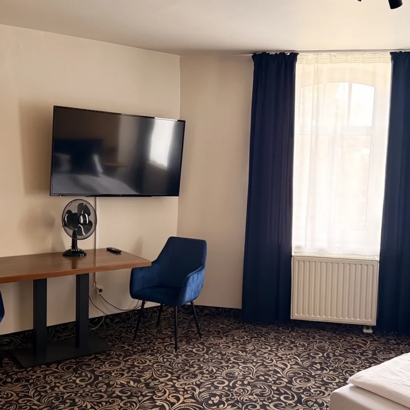 Sitzbereich im Doppelzimmer des Hotel In Amberg mit Tisch, zwei blauen Sesseln und Fernseher